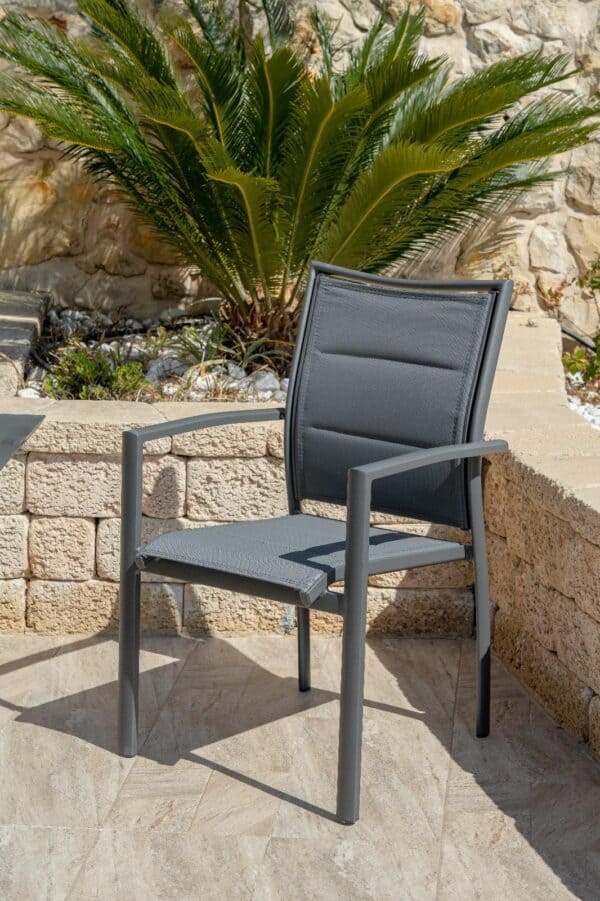 כיסא אלומיניום דגם ליאת בצבע שמנת עם ידיות במרפסת מרוצפת לצד קיר אבן ודקל ירוק.